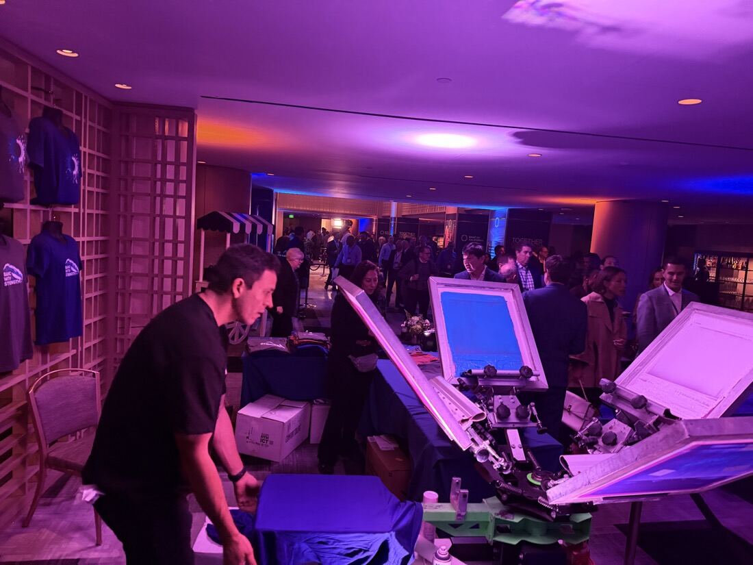 Evening party crowd around live shirt printing stations in a lounge