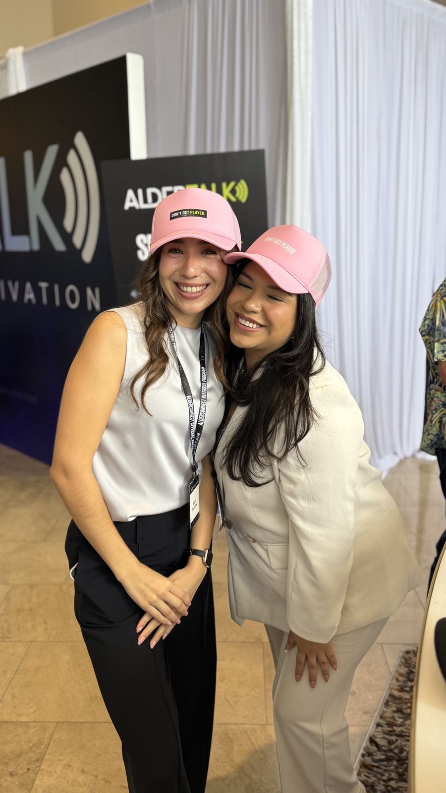 Two friends hugging and laughing in matching pink trucker hats customized at a Merch Troop station